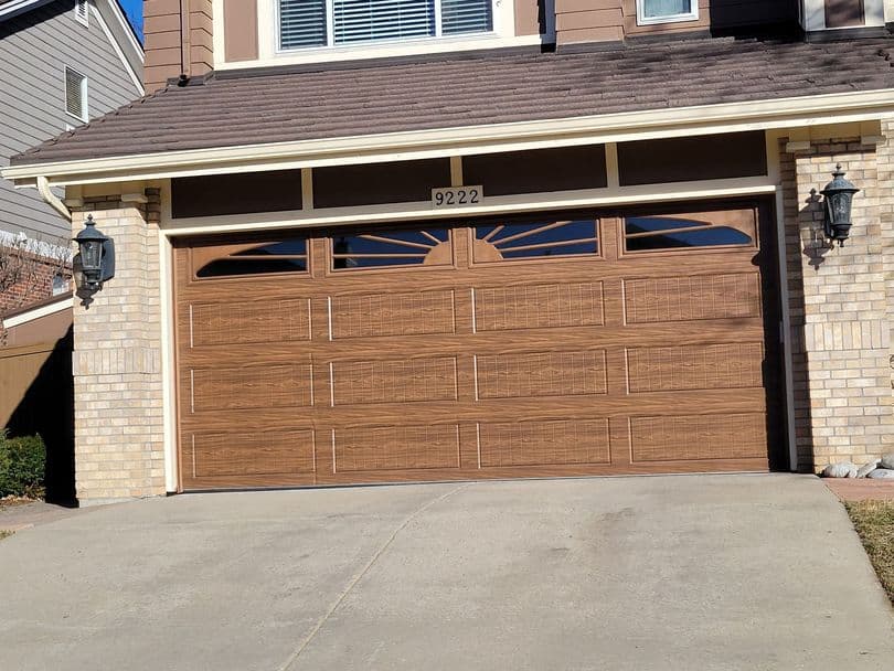Raised panel steel garage door with a wood grain finish and sunburst window pattern